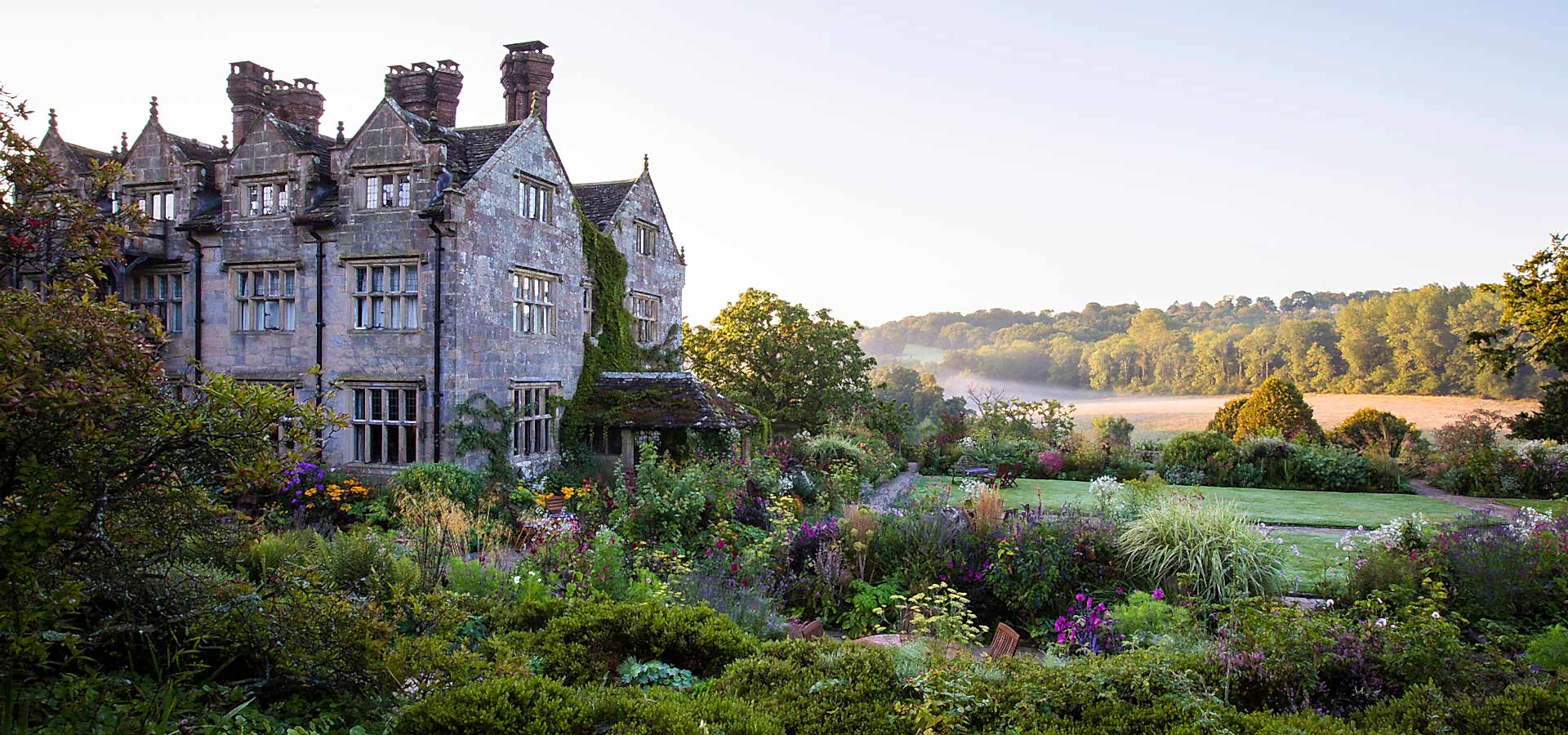 Gardens at dawn with mist over lawns and trees at Gravetye Manor country hotel in West Sussex.