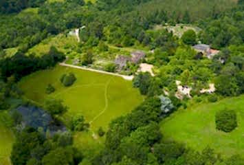 Ariel view of Gravetye Manor and the grounds and courtyard in spring with green forests surrounding.