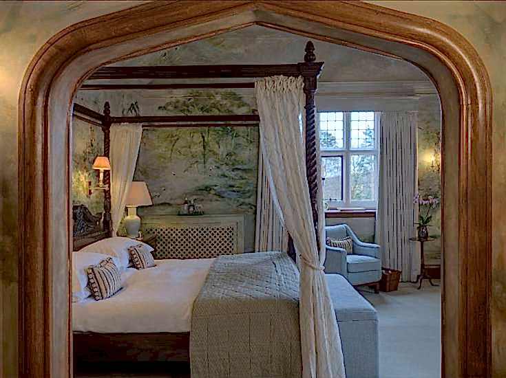 Four poster bed with crisp linens and floral textiles. Country house suite at Gravetye Manor West Sussex.