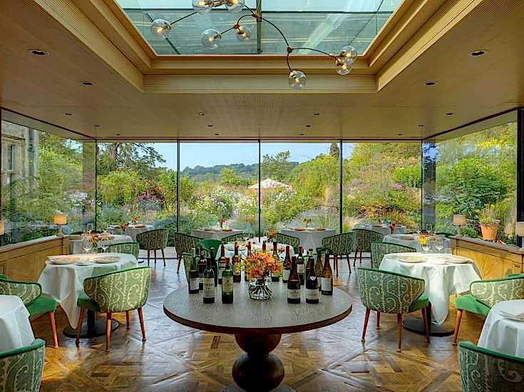Elegant dining room at Gravetye Manor, West Sussex with glass-walls overlooking the gardens.