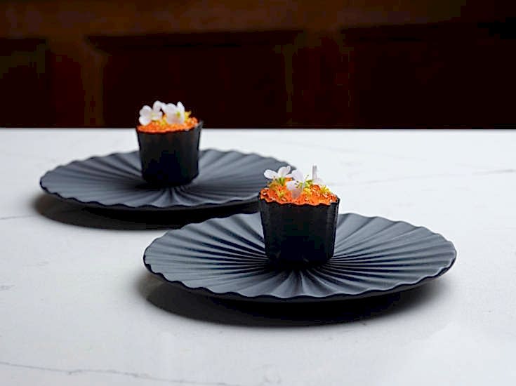 Small gourmet meal with green garnish on black decorated plates served at Gravetye Manor West Sussex.