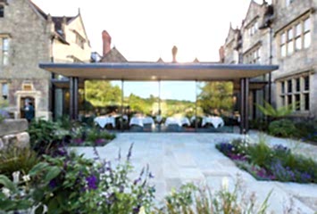 Exterior view of the glass-walled dining room at Gravetye Manor in West Sussex, overlooking landscaped gardens and countryside views.